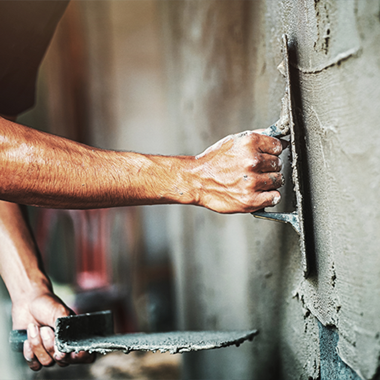 Alt text: Renovation insurance — close-up of a worker’s hands smoothing wet plaster on an interior wall with a trowel and hawk
