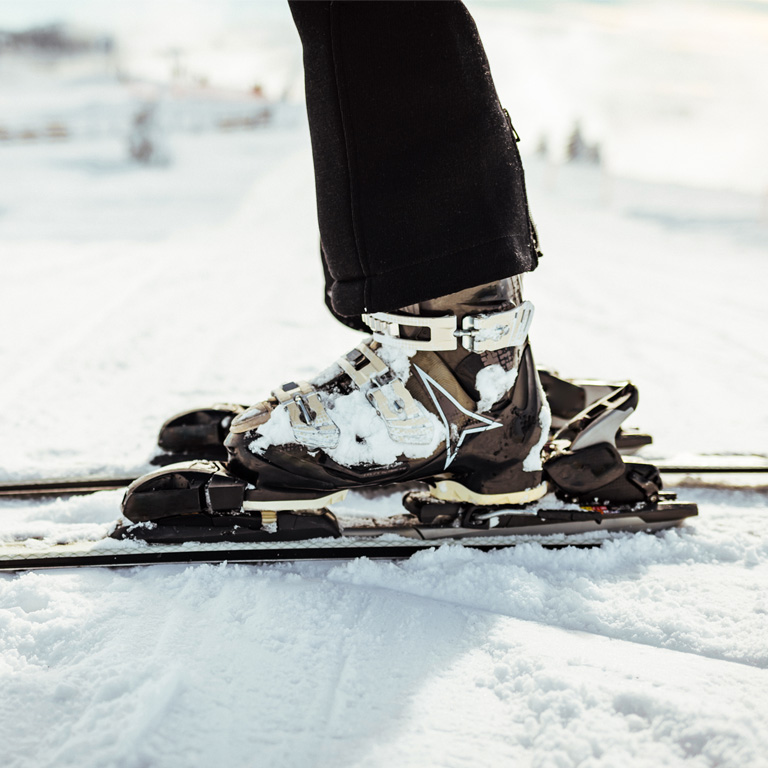 Close-up of a person wearing ski boots and skis on snow, perfect for family ski holidays and winter outdoor activities